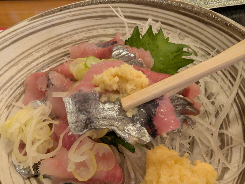 箸でおろし生姜を添えていただく、ニシンのお刺身のアップ。脂の乗った銀色の皮目と、鮮やかな身の質感が食欲をそそる一枚。