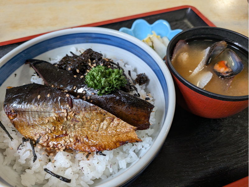 「民宿 青塚食堂」のにしん丼。ご飯の上に大きなニシンの甘露煮が2枚乗り、白胡麻とパセリが添えられている。横には稚貝の味噌汁が並ぶ。