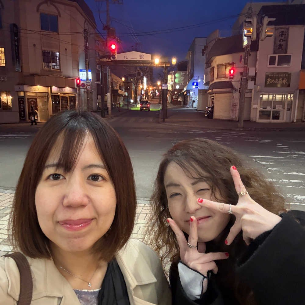 夜の小樽の街並みをバックに笑顔でピースサインをする女性二人のセルフポートレート