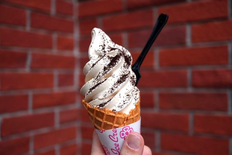 レトロな赤レンガの壁をバックに、コーヒー粉末がトッピングされた「可否茶館」のコーヒーソフトクリームを手に持っている写真