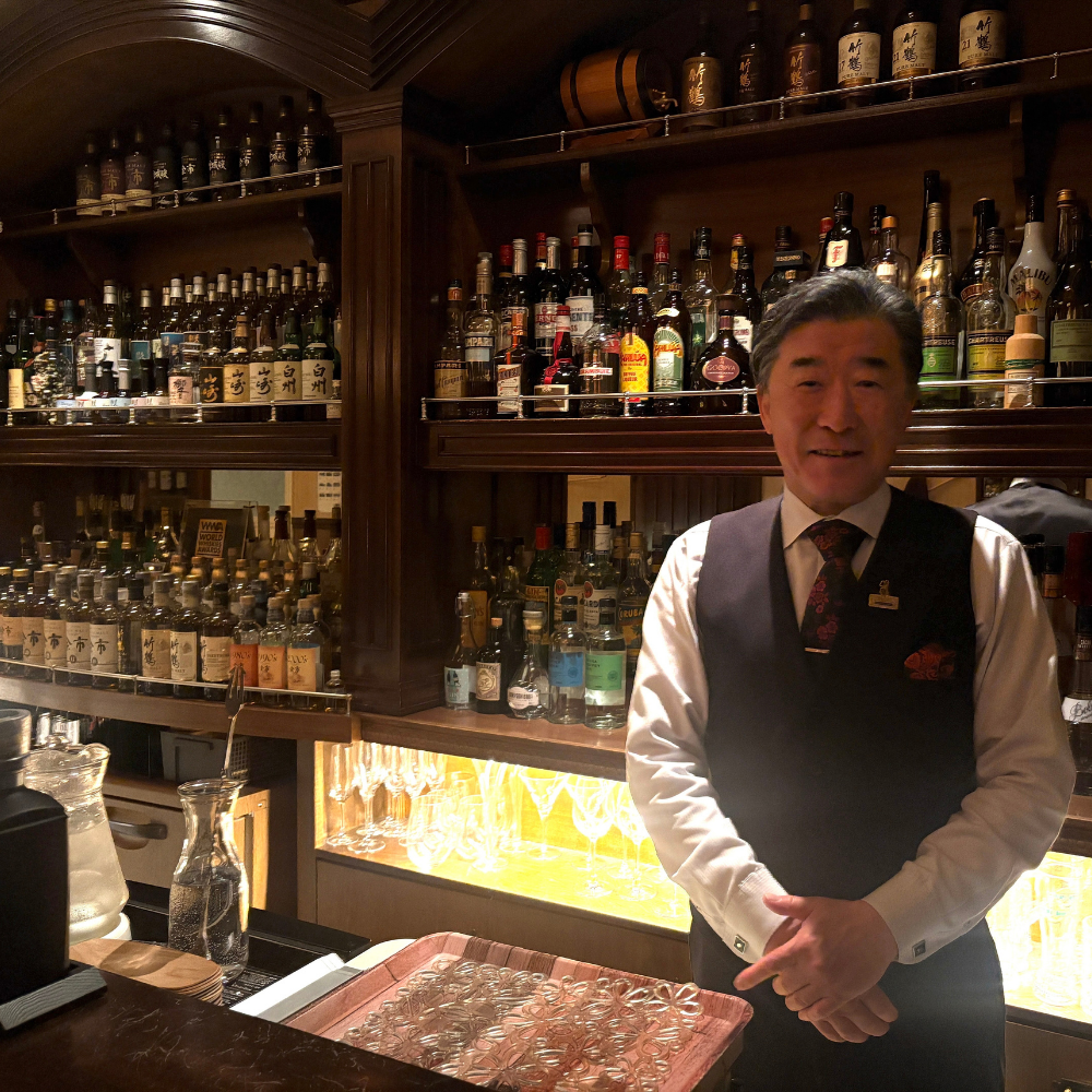 白いシャツにベストを着用し、カウンターの中で静かに佇む「THE BAR HATTA」のバーテンダー