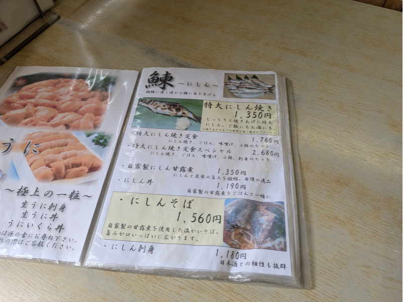 「民宿 青塚食堂」のメニュー表。「特大にしん焼き」や「にしんそば」、「にしん刺身」など、ニシン料理のラインナップと価格が記載されている。