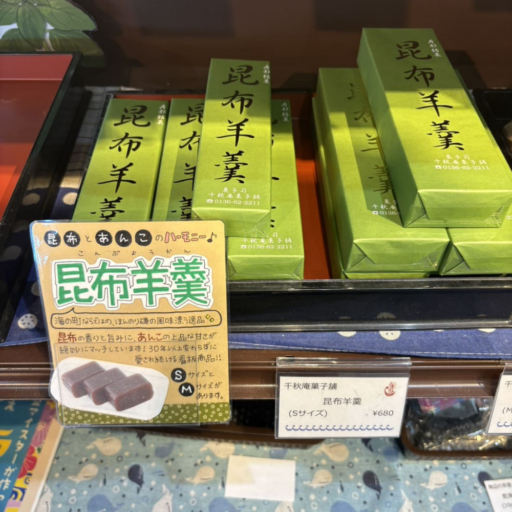 緑色の箱に入った千秋庵菓子舗の「昆布羊羹」が棚に並べられている様子。「昆布とあんこのハーモニー♪」や「30年以上変わらずに愛され続ける看板商品」と書かれたポップと、価格案内（Sサイズ 680円）が添えられている。