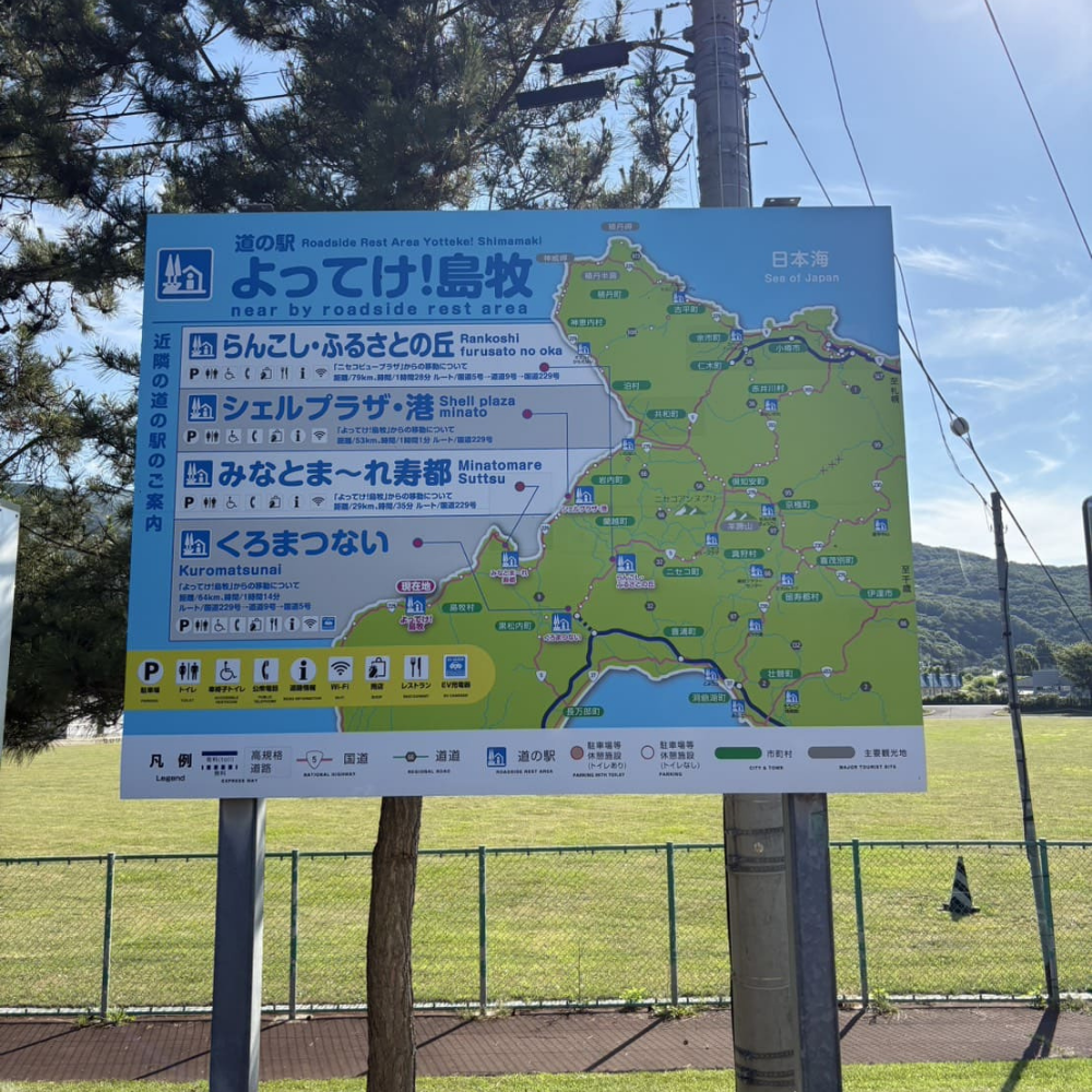 「道の駅 よってけ！島牧」の敷地内に設置された広域案内看板。近隣の道の駅（らんこし・ふるさとの丘、シェルプラザ・港、みなとま～れ寿都、くろまつない）の位置関係や移動時間・距離が、後志エリアの地図とともに描かれている様子。