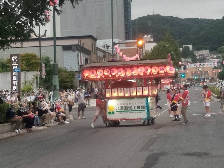 背景にJR小樽駅が見える駅前通りで、赤い提灯が灯る潮太鼓の山車を引いて進む潮ふれこみの隊列