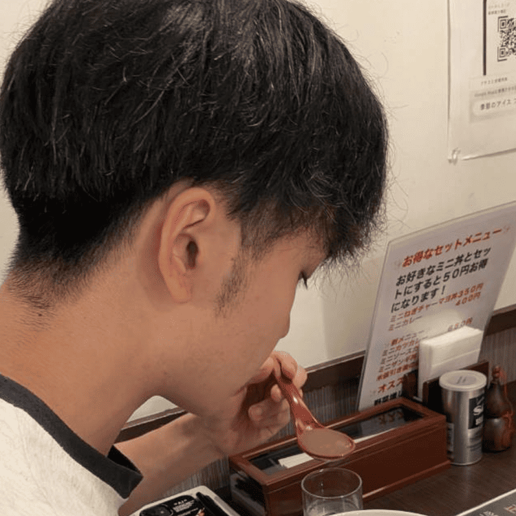 「らーめん むくげ」の店内で、レンゲですくったラーメンのスープを味わう大学生