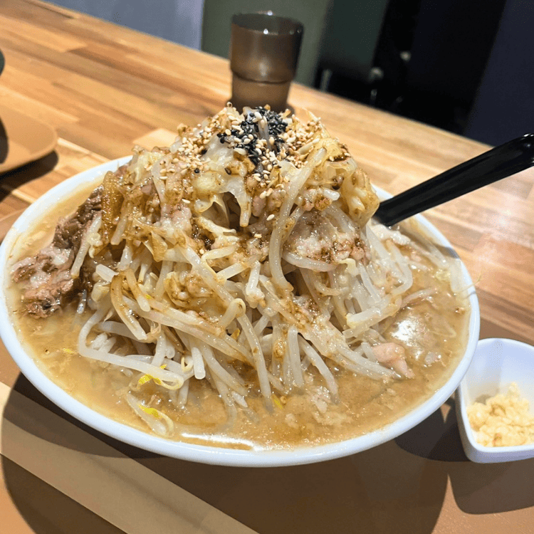 「NOODLE rafe」のガッツリ系ラーメン。丼いっぱいに山盛りされたもやしと背脂、ゴマがトッピングされ、横には刻みニンニクが添えられている