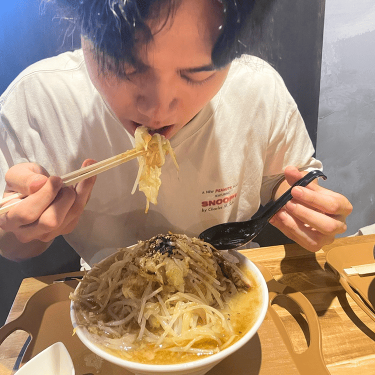 「NOODLE rafe」の店内で、山盛りにトッピングされた野菜を豪快に口へ運ぶ大学生