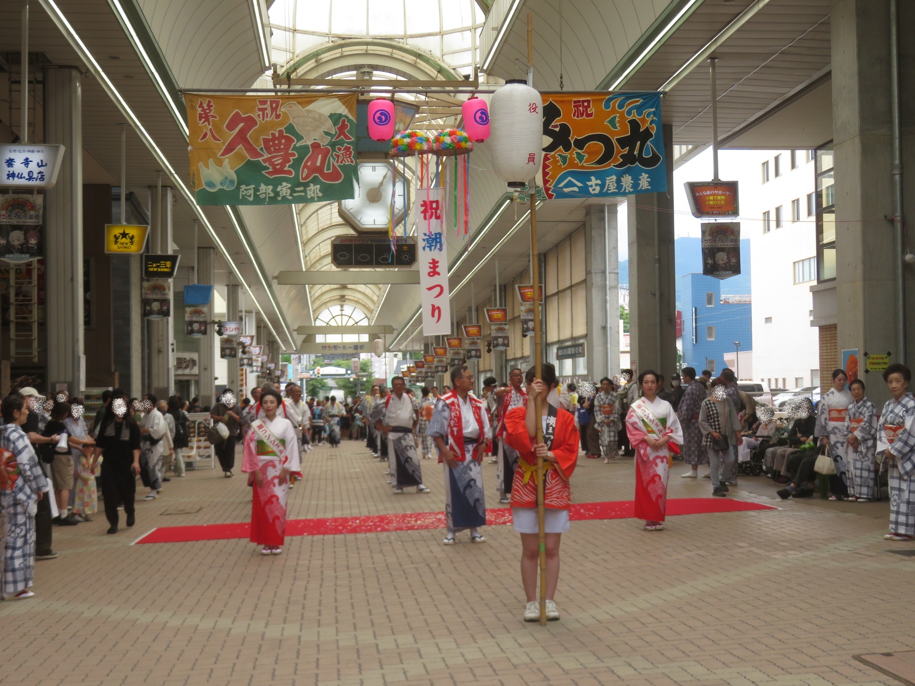 大漁旗や「祝 潮まつり」のくす玉が飾られたサンモール一番街アーケード内で、提灯を持った先頭の女性を囲むように潮コンシェルジュや関係者、踊り手たちが並び出発する様子