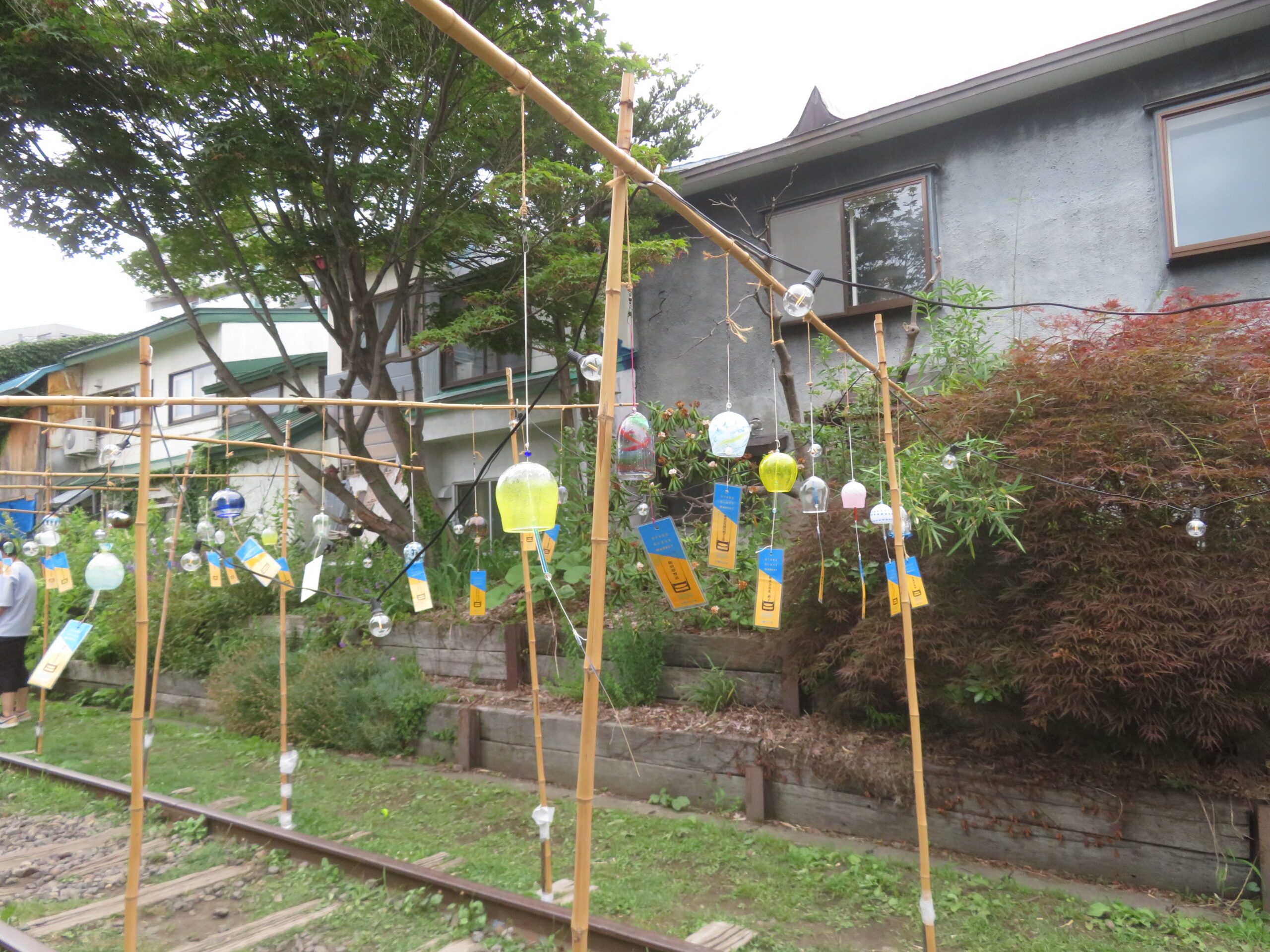 小樽がらす市の会場(旧手宮線)にて、竹で組まれた枠に透明や黄色など色とりどりの風鈴がいくつも吊り下げられ、短冊が揺れる涼しげな装飾の様子