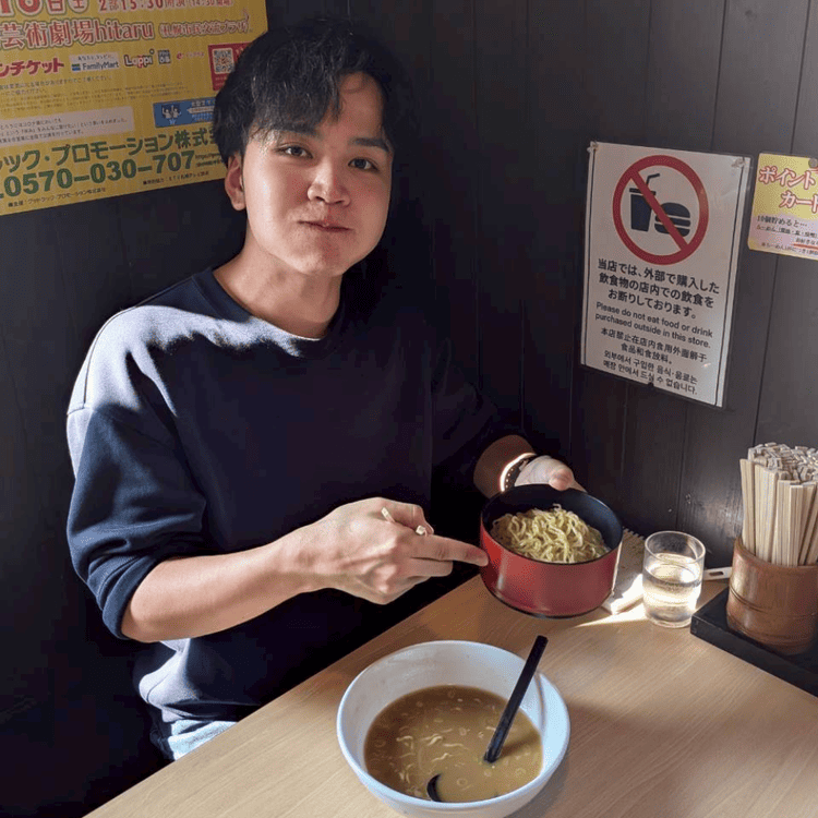 「おたる蔵屋」の店内で、追加注文した替え玉の器を手に持ち、嬉しそうな表情を見せる大学生