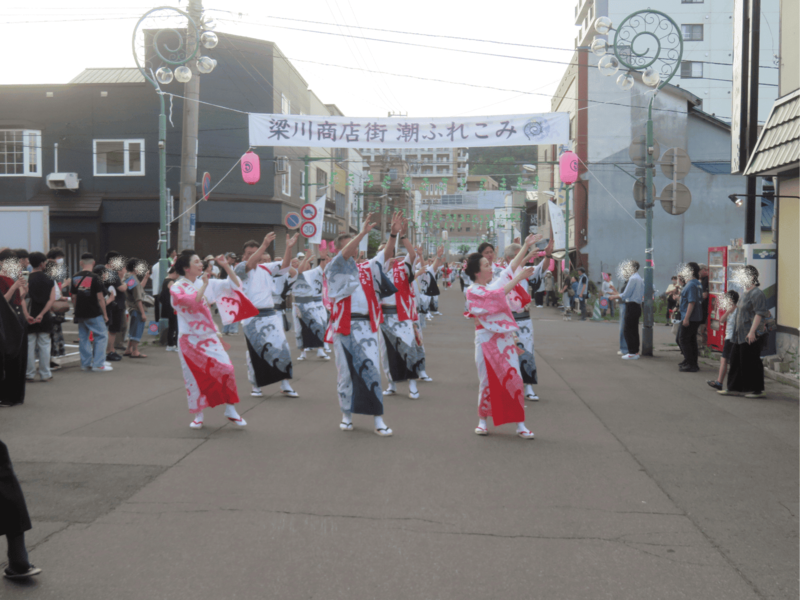 「梁川商店街 潮ふれこみ」の横断幕が掲げられた通りで、揃いの浴衣を着た参加者たちが潮音頭に合わせて踊り歩く様子